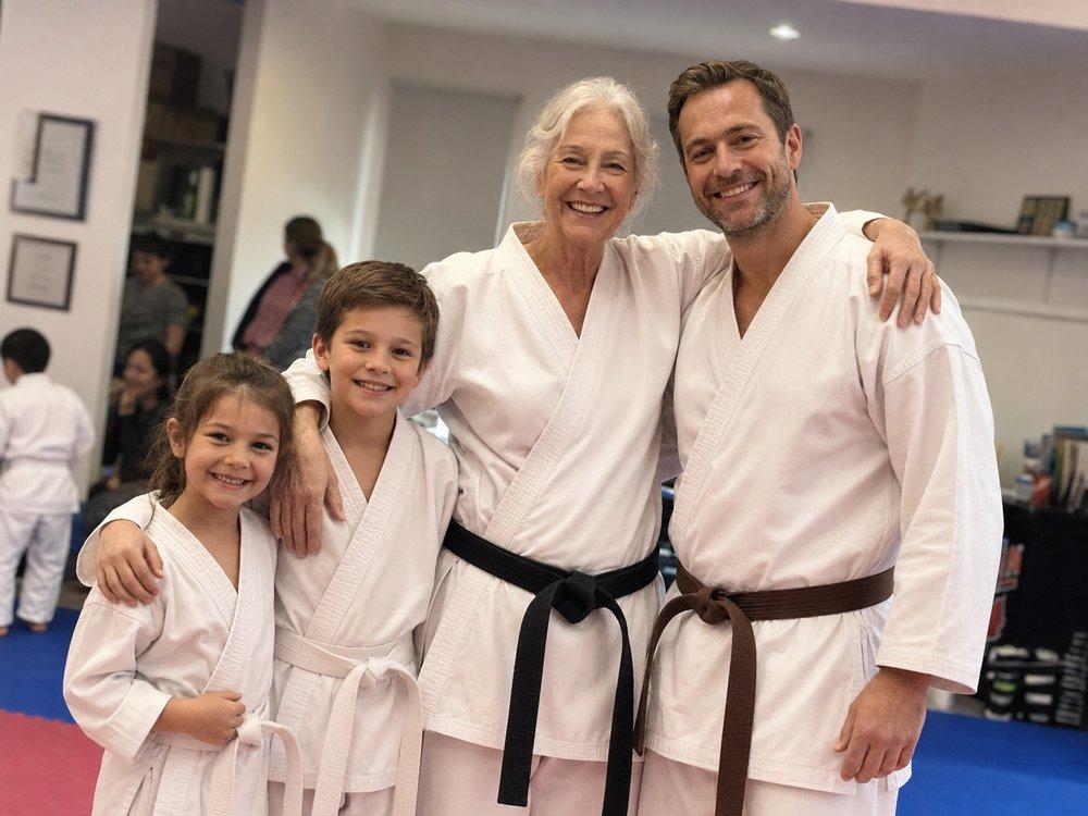 Karate students of every age — a young girl, a young boy, an older black belt, and an adult brown belt, together at the dojo